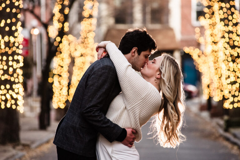 Engaged couple kisses on Addison street with lights behind them