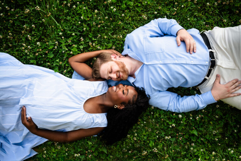 Expectant couple lying in a clover field in Bartram's Garden